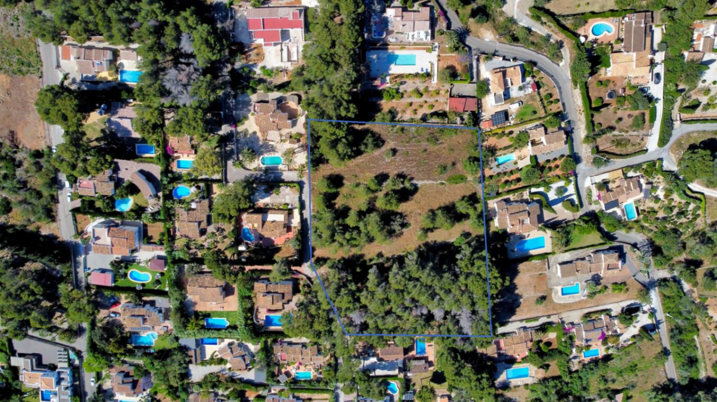 Vista aérea perimetrada de la amplia parcela llana en Jávea, destacando su densa vegetación autóctona y su ubicación privilegiada rodeada de villas residenciales.