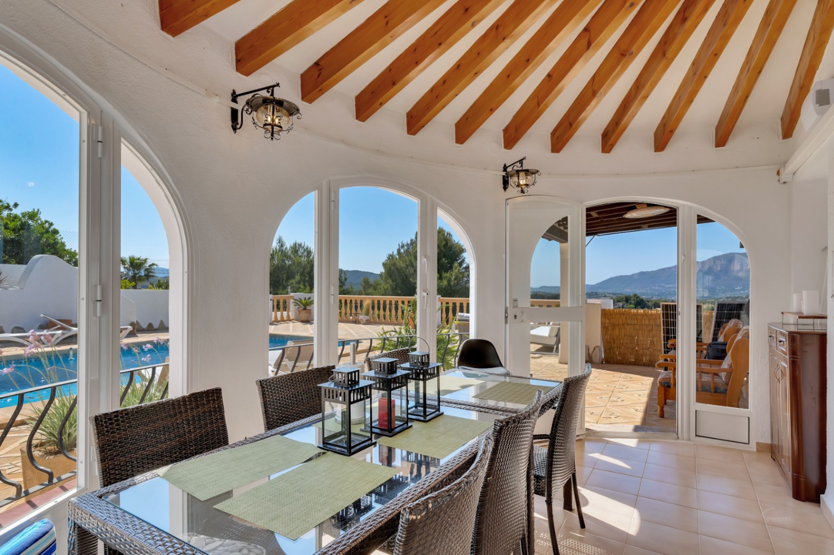 Comedor cubierto con vigas de madera radiales, grandes ventanales en arco con vistas a la piscina y al Montgó, y acceso directo a la terraza exterior.