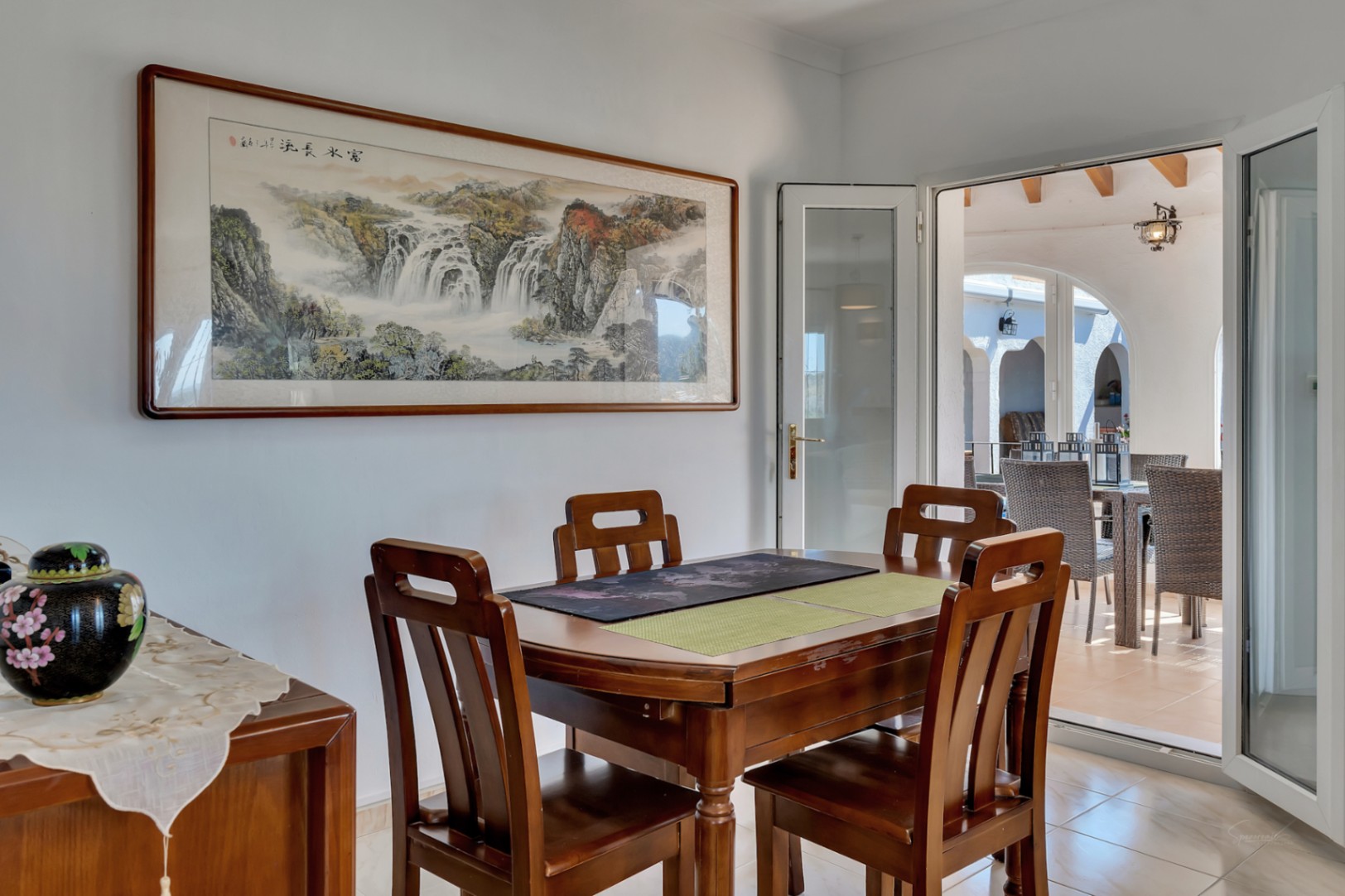 Comedor interior con mobiliario de madera maciza y acceso directo a la terraza. La estancia cuenta con un gran cuadro decorativo y suelos cerámicos claros.