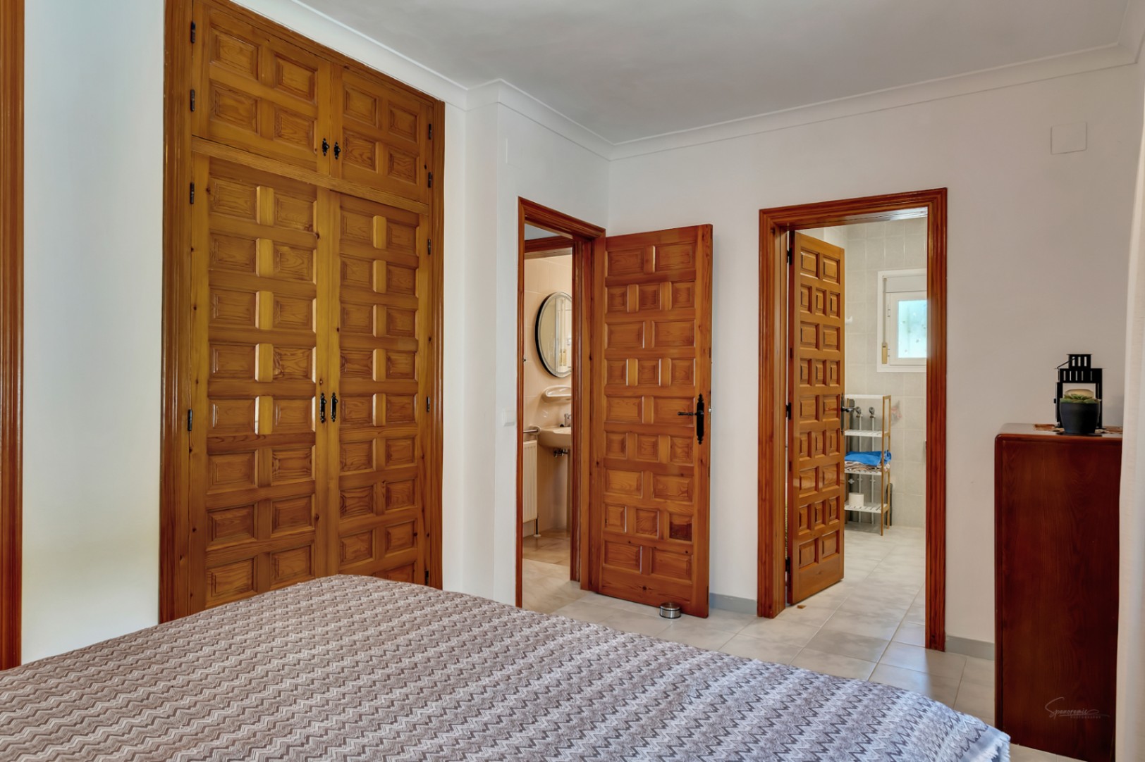 Dormitorio con amplios armarios empotrados de madera tallada y acceso directo a baños privados, destacando la carpintería tradicional y suelos cerámicos claros.