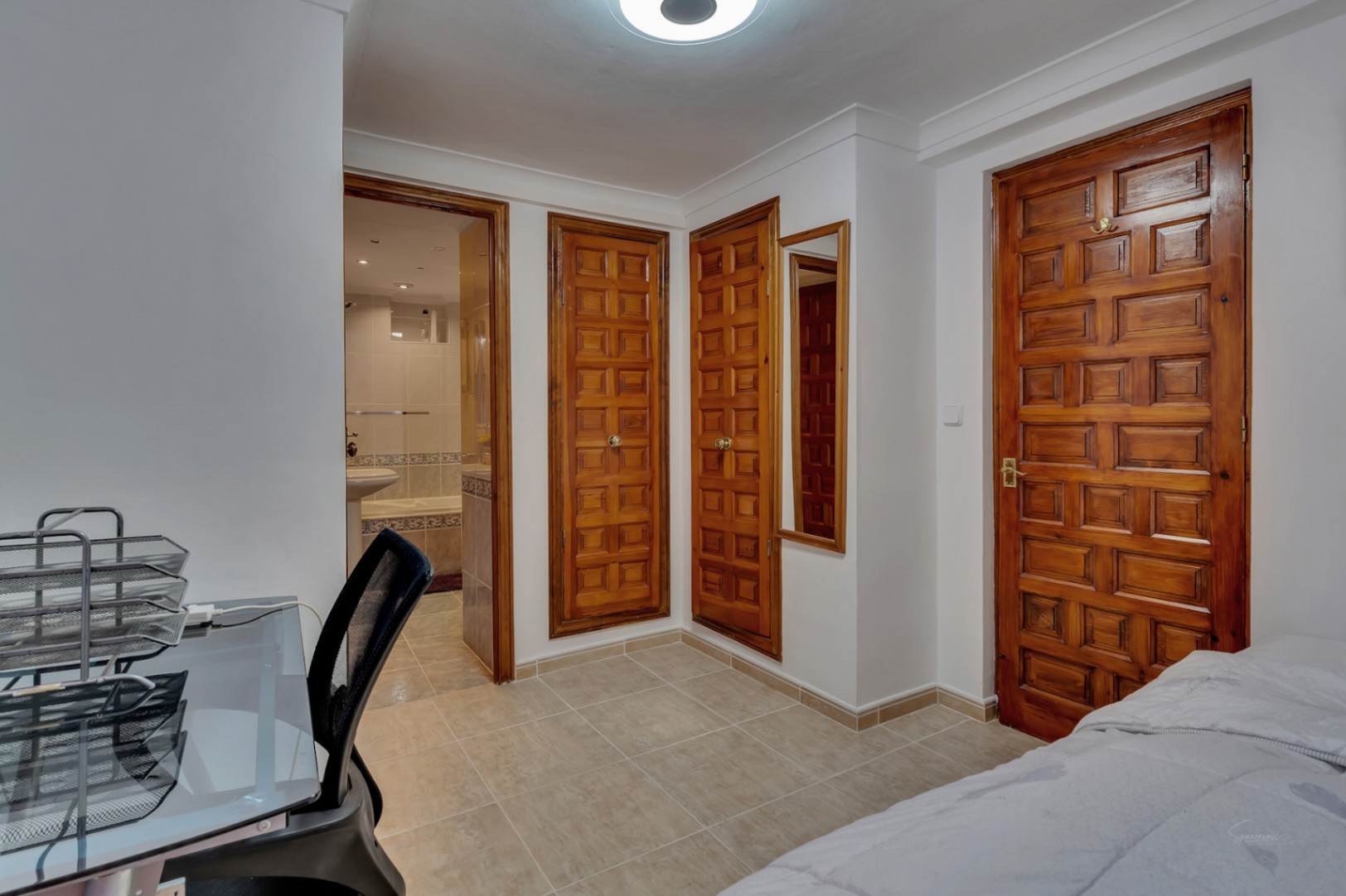 Dormitorio con armarios empotrados de madera noble, suelos cerámicos y acceso directo a un baño en suite. Incluye una zona de escritorio funcional.