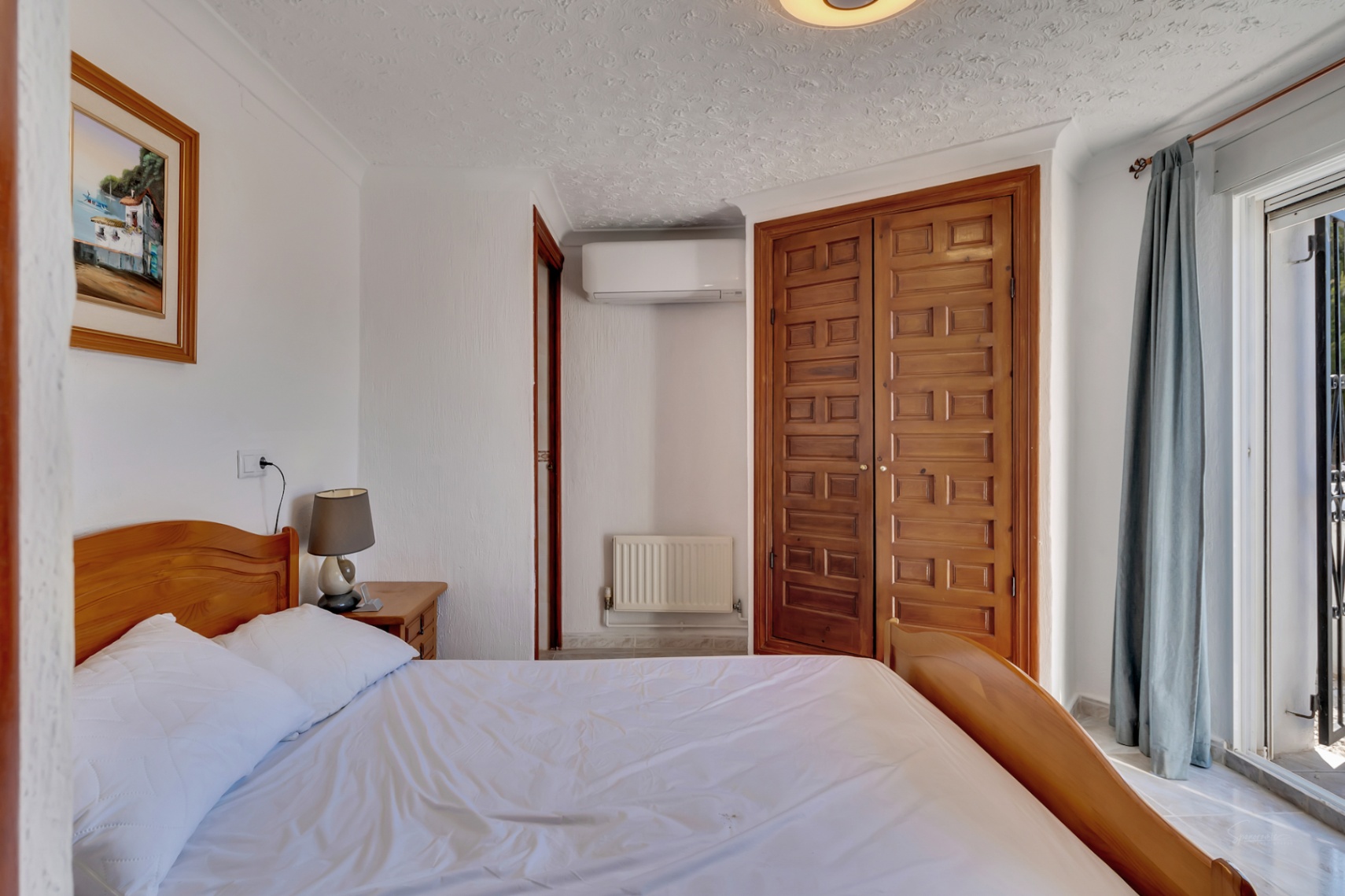 Dormitorio luminoso con armario empotrado de madera tallada, aire acondicionado y acceso directo a la terraza mediante ventanal.
