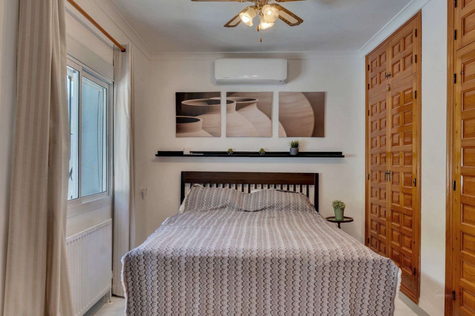 Dormitorio luminoso con armarios empotrados de madera tallada, aire acondicionado, ventilador de techo y ventana de doble acristalamiento con radiador.