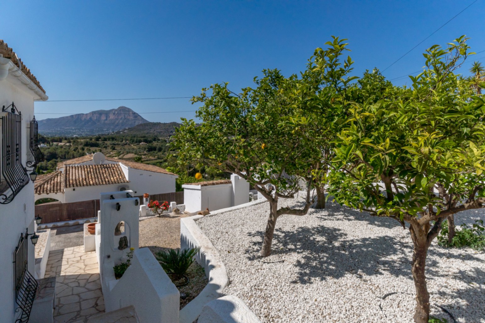 Jardín mediterráneo de bajo mantenimiento con grava blanca y cítricos, ofreciendo vistas despejadas al macizo del Montgó desde una zona exterior elevada.
