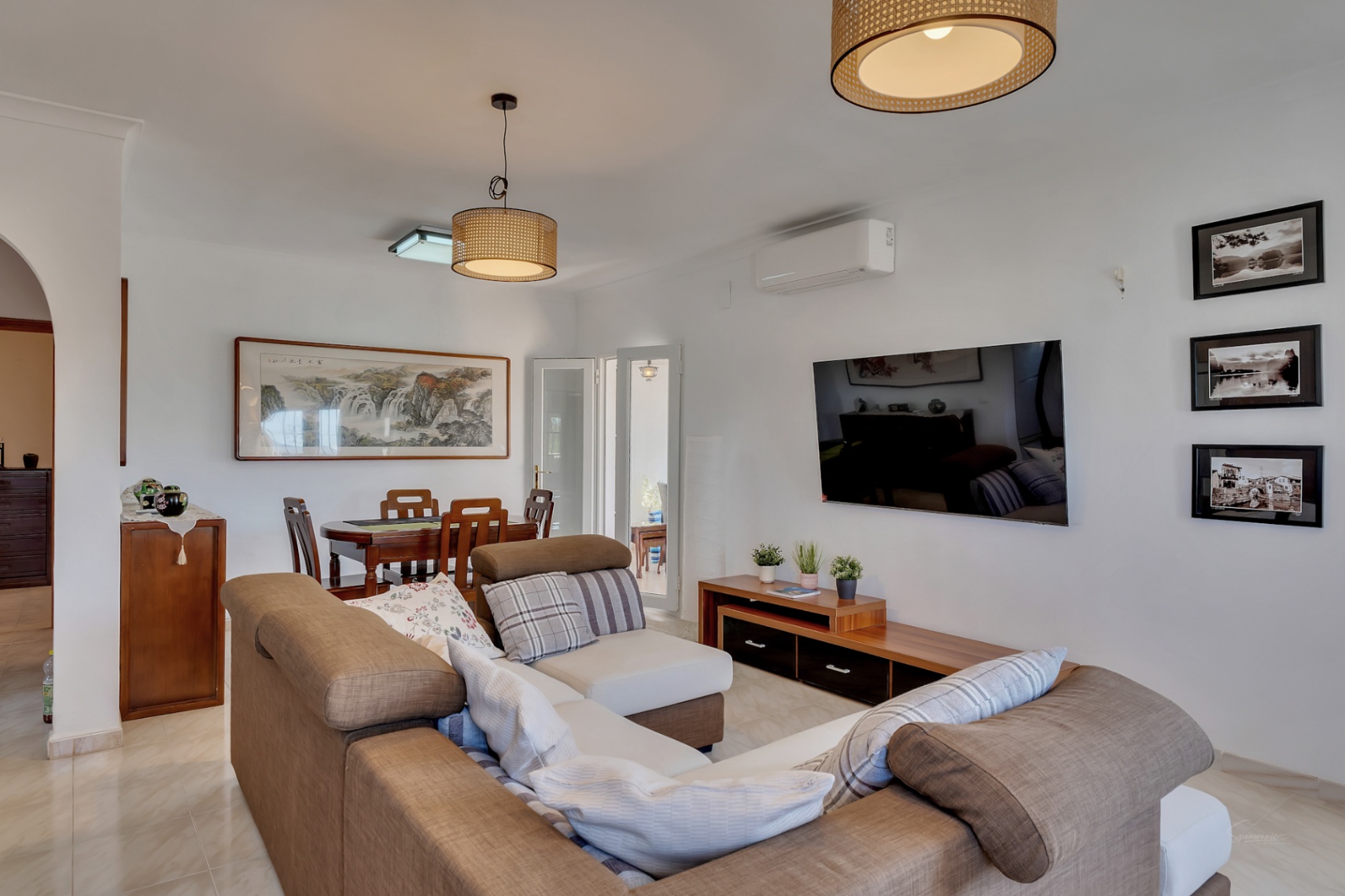 Salón comedor diáfano con sofá en L, mesa de madera y lámparas de mimbre. Dispone de aire acondicionado, suelos cerámicos y decoración de inspiración natural.