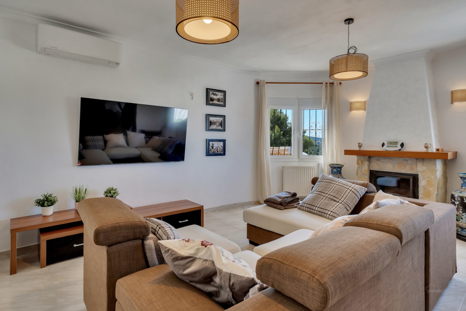 Salón luminoso con chimenea de piedra, aire acondicionado y lámparas de fibras naturales. Dispone de un amplio sofá rinconera y televisión de pantalla plana.