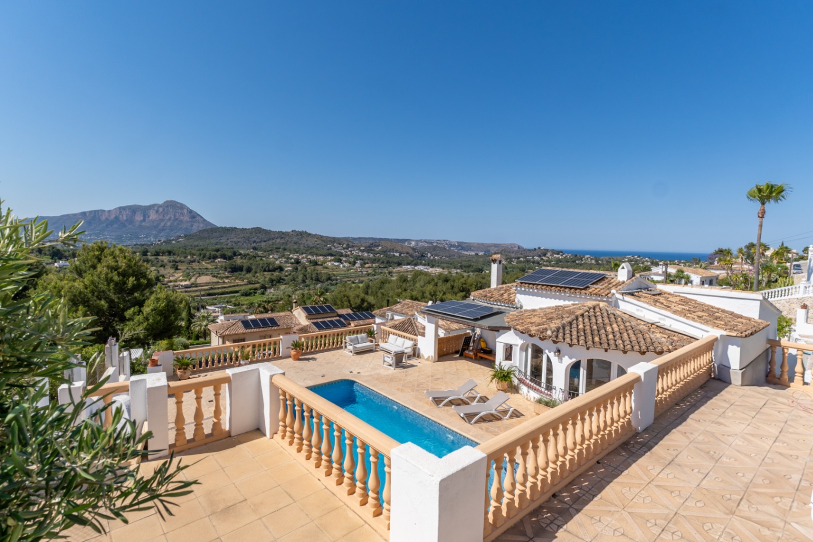 Vista panorámica desde la terraza superior que muestra la piscina, la instalación de placas solares y las vistas abiertas al Montgó y al mar Mediterráneo.