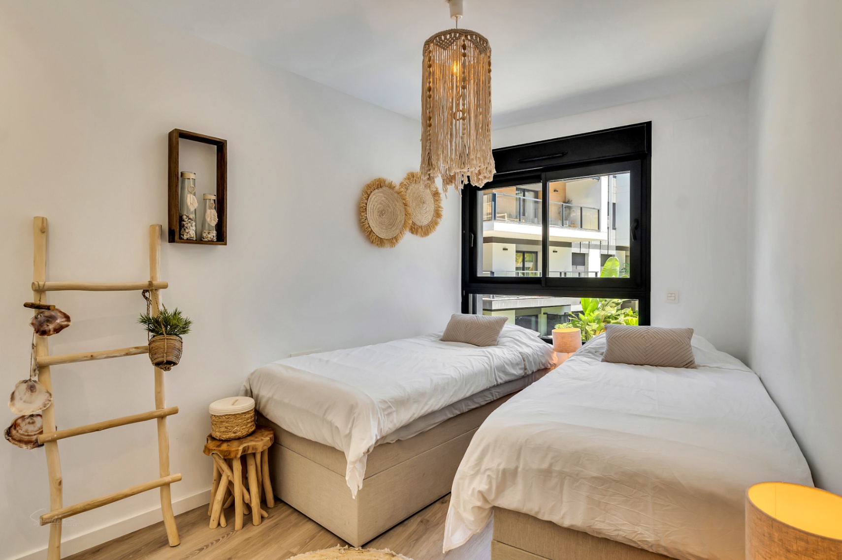 Dormitorio con dos camas individuales, decoración de inspiración mediterránea y gran ventanal de carpintería negra con vistas despejadas a la urbanización.
