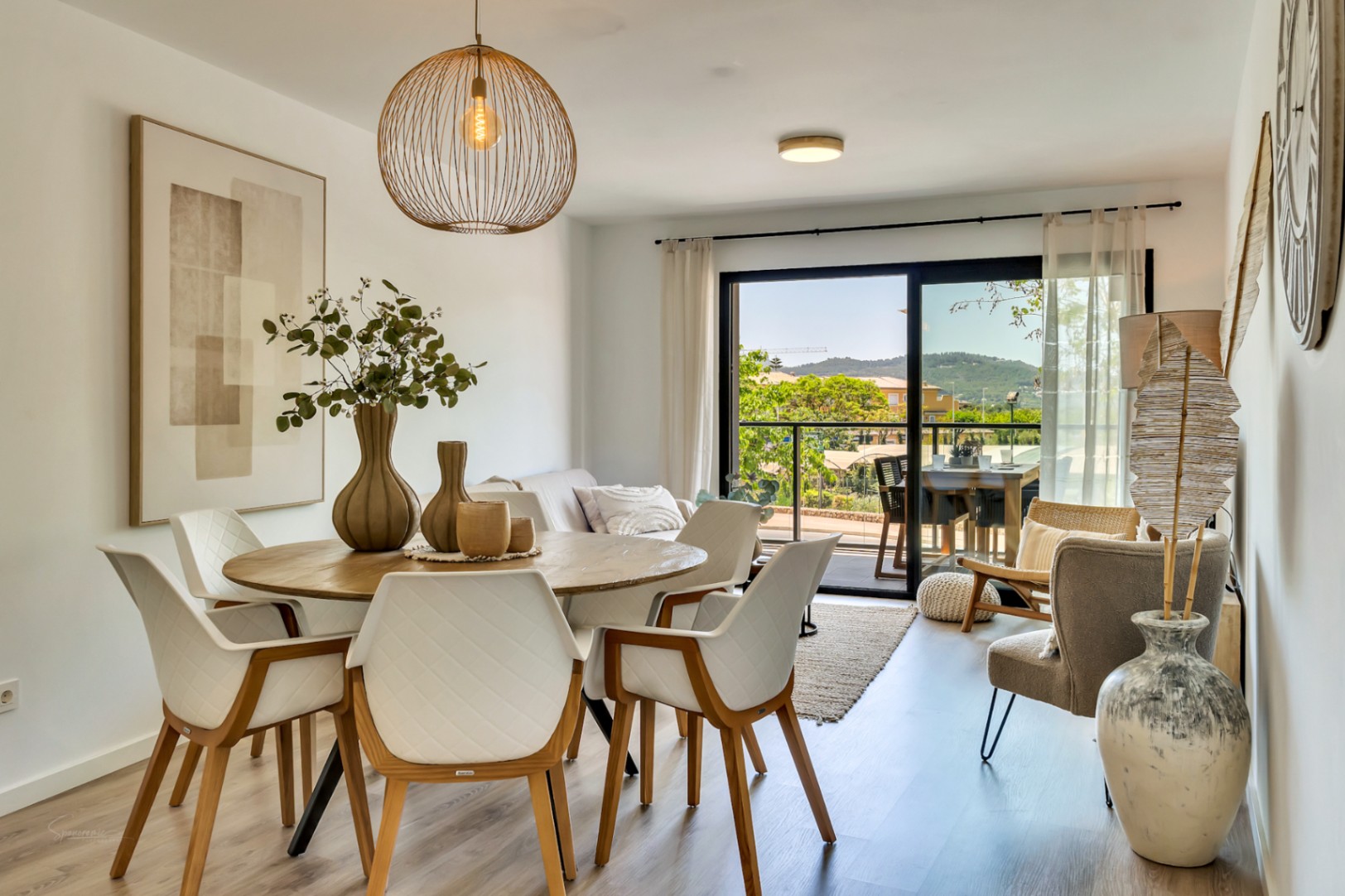 Salón-comedor de concepto abierto con mobiliario de madera, sillas acolchadas blancas y acceso directo a la terraza con vistas despejadas a la montaña.