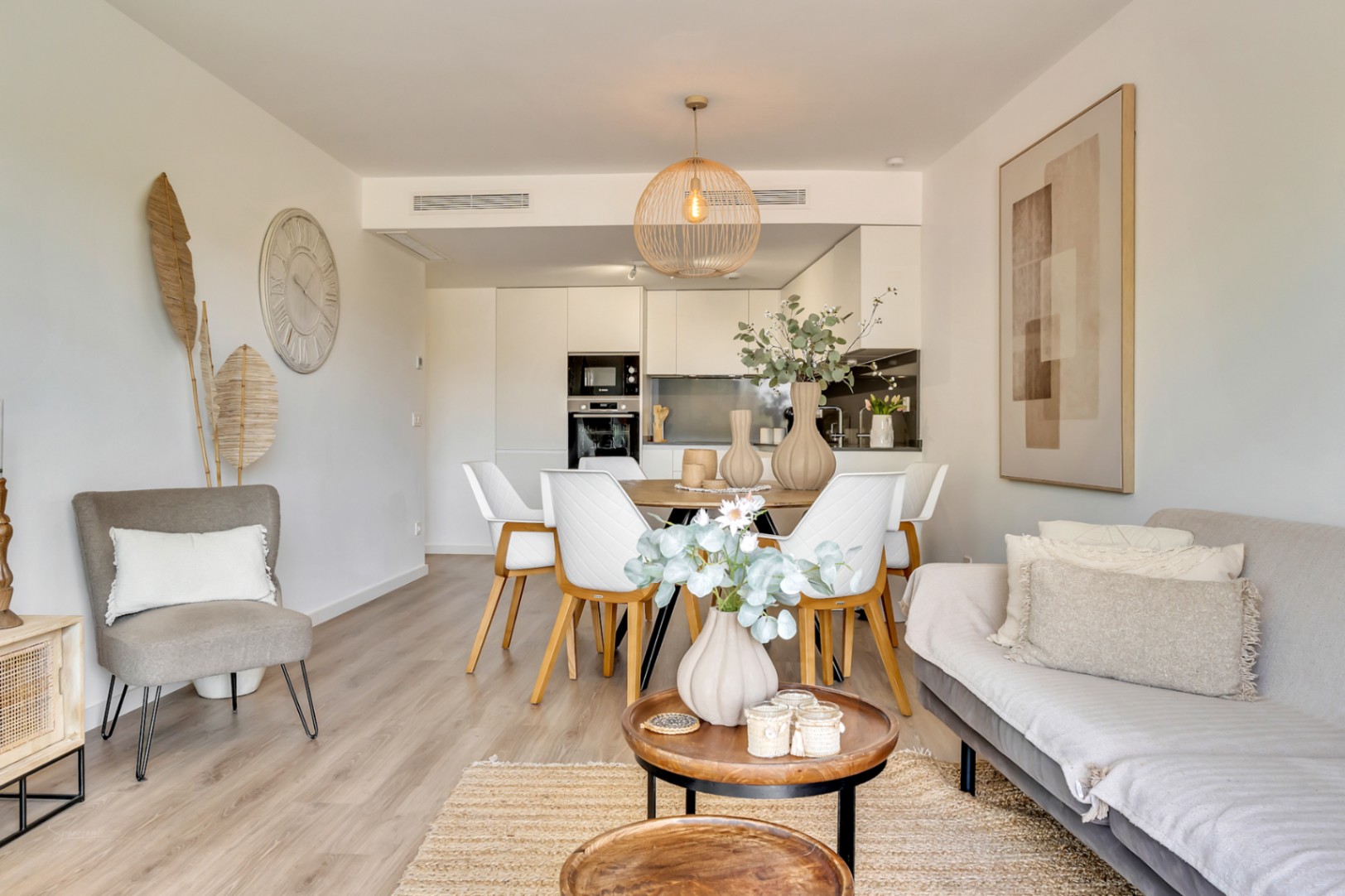 Salón-comedor de concepto abierto con suelos de madera clara, mobiliario contemporáneo en tonos neutros y cocina integrada con armarios blancos y electrodomésticos encastrados.