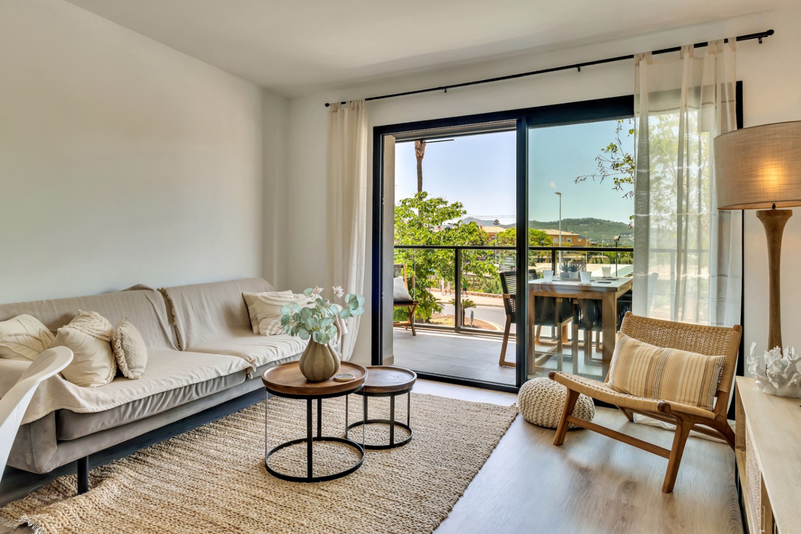Salón luminoso con mobiliario en tonos neutros, suelos de madera y acceso directo a una terraza privada con zona de comedor exterior y vistas despejadas.
