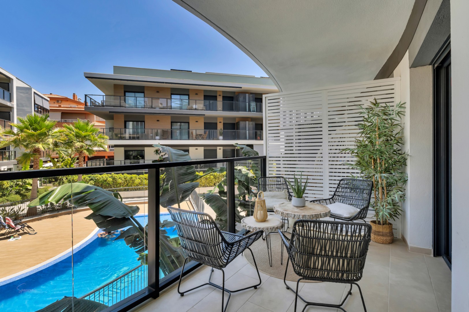 Terraza privada con barandilla de cristal, mobiliario de diseño y vistas despejadas a la piscina comunitaria y zonas ajardinadas del complejo residencial.
