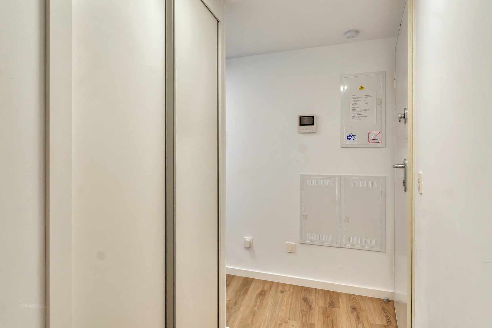 Vestíbulo de entrada con suelos de madera, armario empotrado blanco y paneles de control integrados en la pared para una estética moderna y funcional.