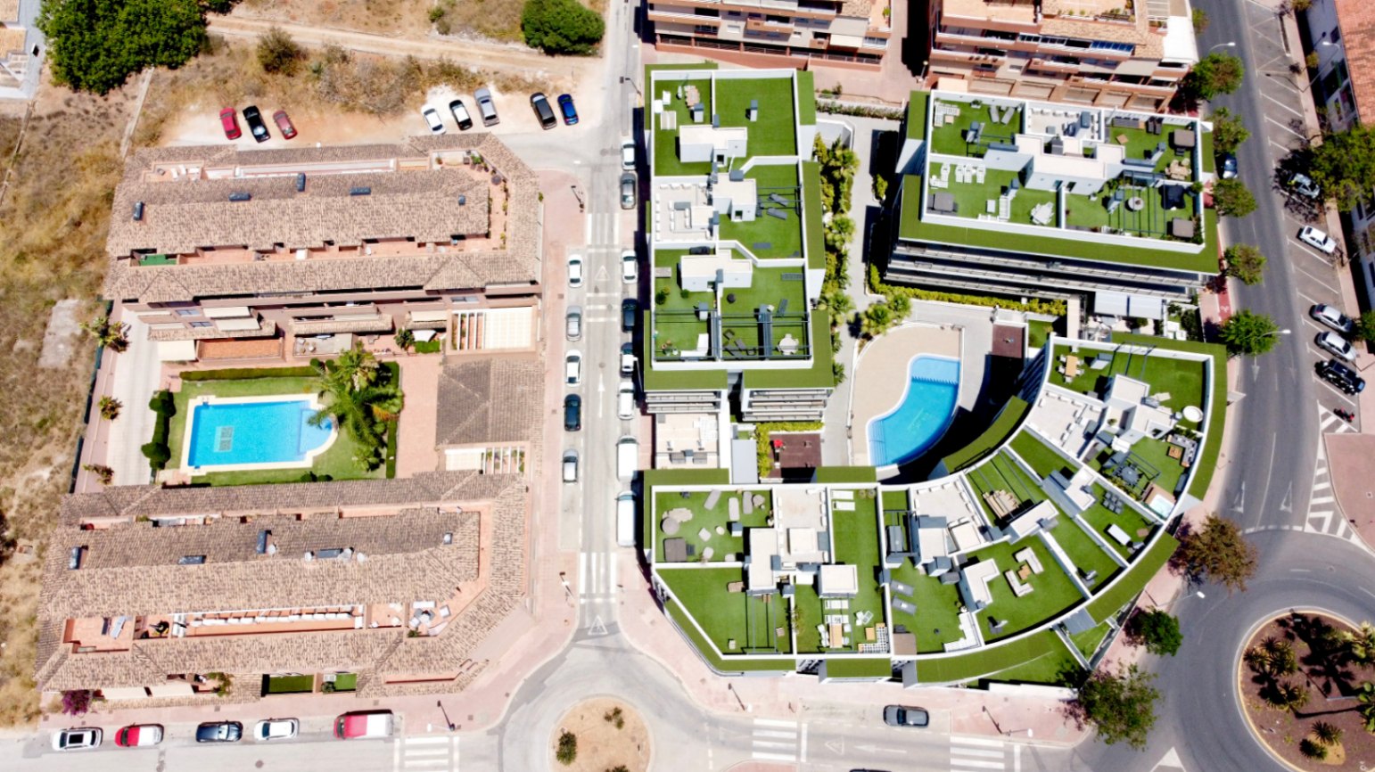 Vista aérea del complejo residencial moderno que destaca por sus azoteas ajardinadas, arquitectura contemporánea y una piscina comunitaria de diseño curvo.