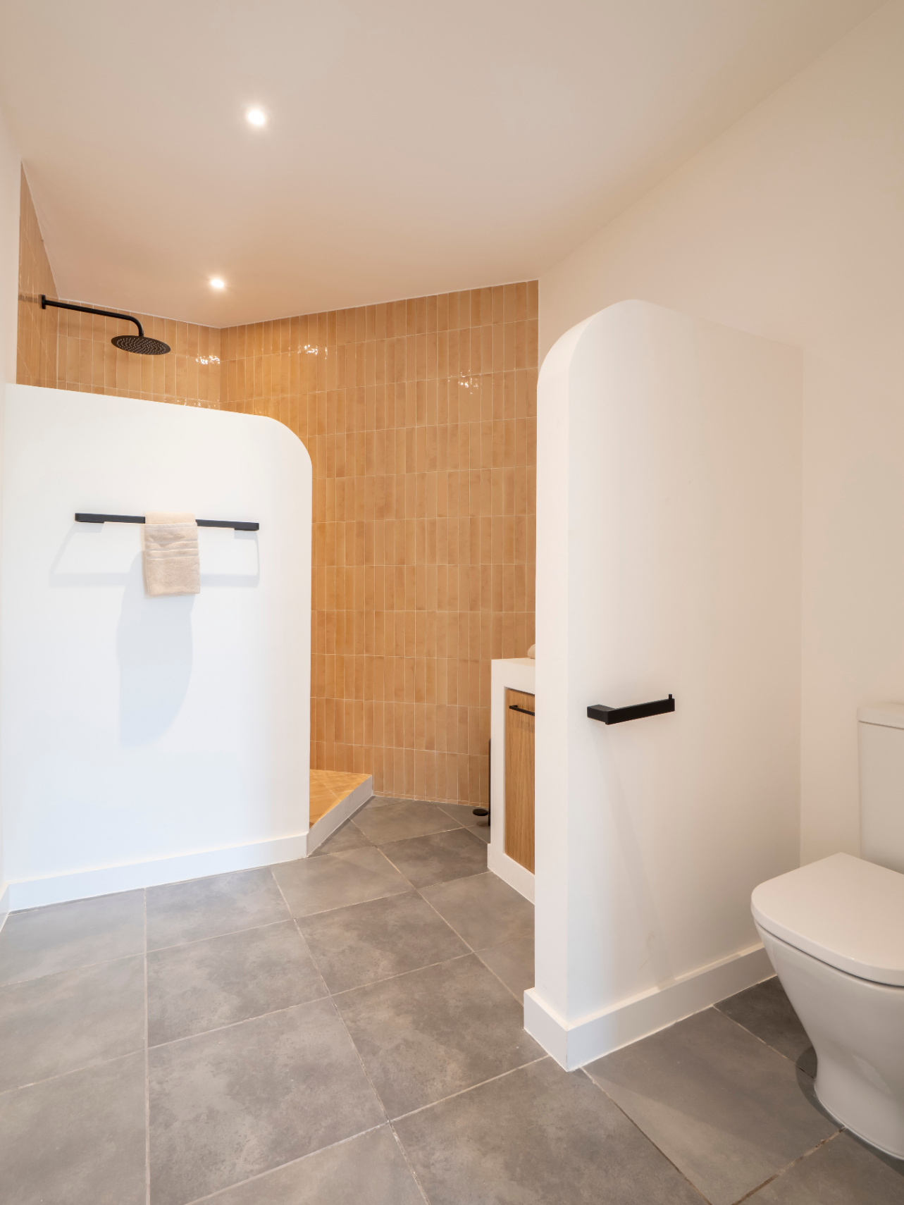 Cuarto de baño con ducha de obra y azulejos color ocre. Mueble de madera y suelo de baldosas grises.
