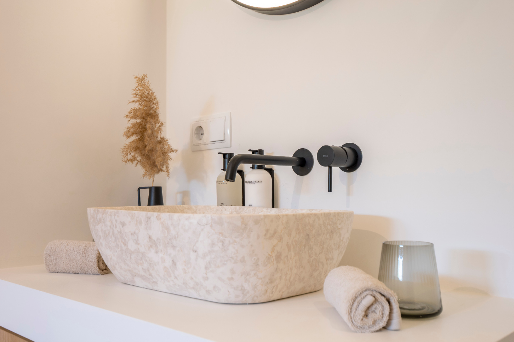 Detalle de baño con lavabo de piedra natural y grifería negra mate. Decoración minimalista y toallas a juego.