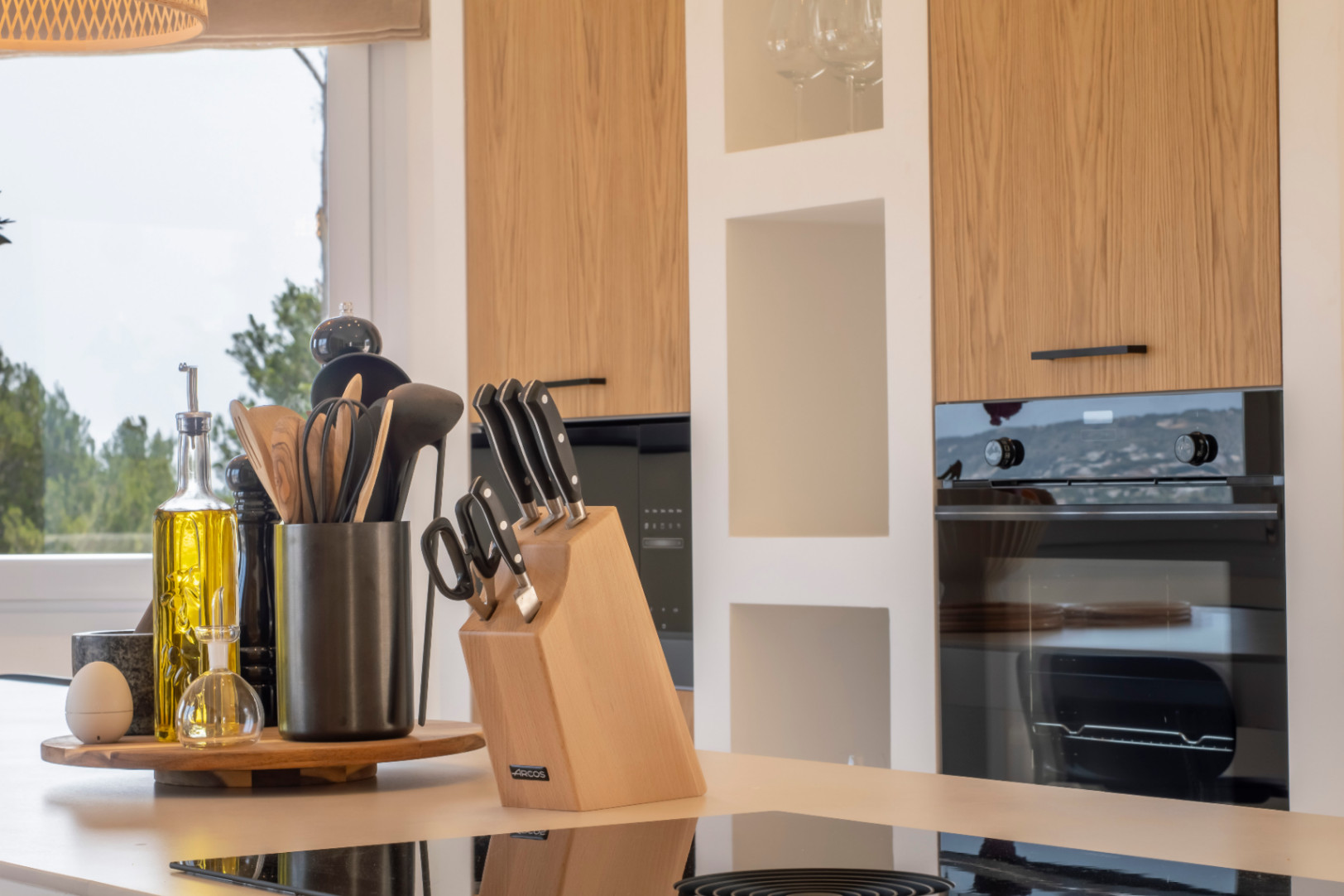Detalle de cocina con encimera reflectante, utensilios de madera y armarios de roble claro.