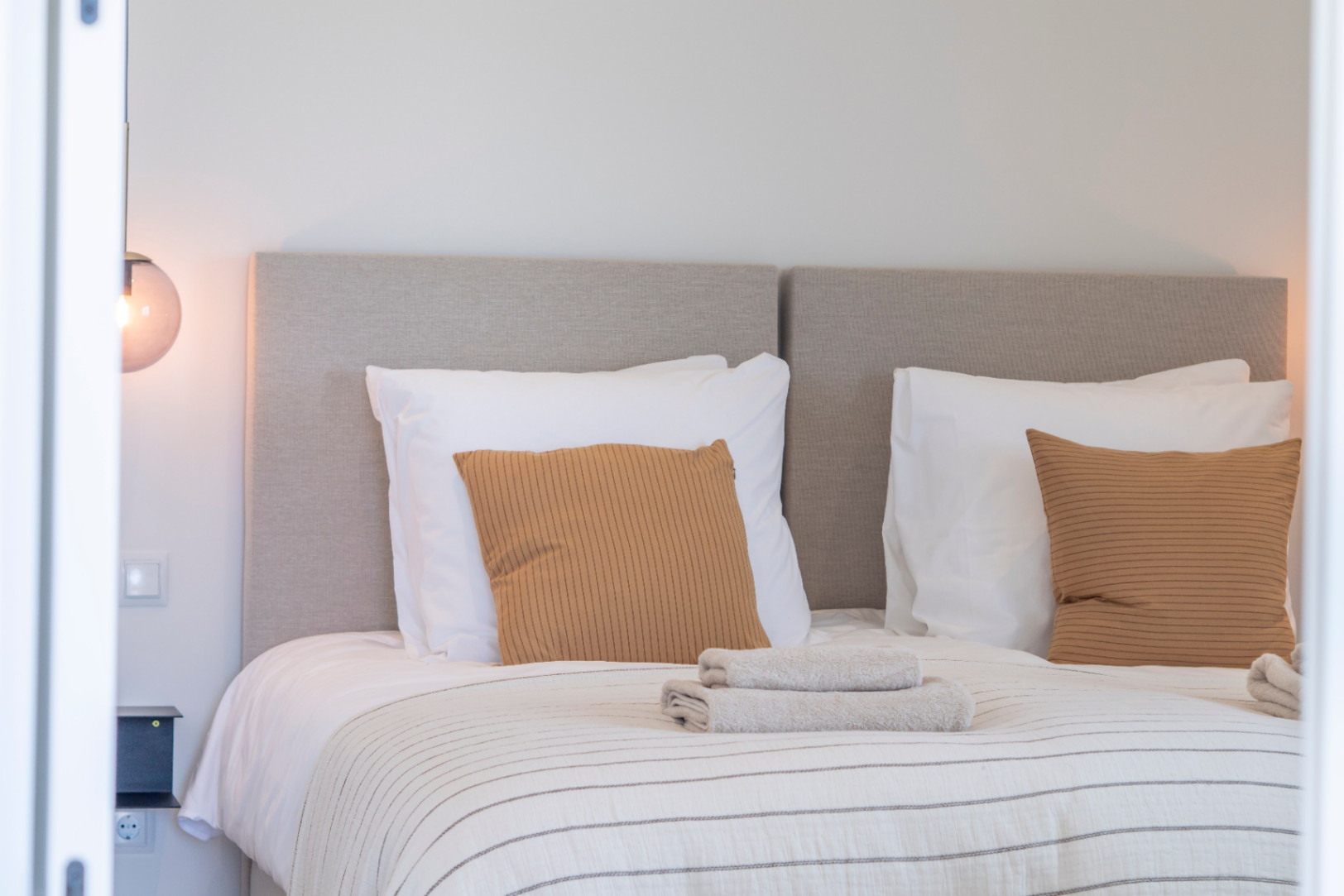 Detalle de dormitorio con cabecero tapizado, almohadas color mostaza y ropa de cama a rayas.