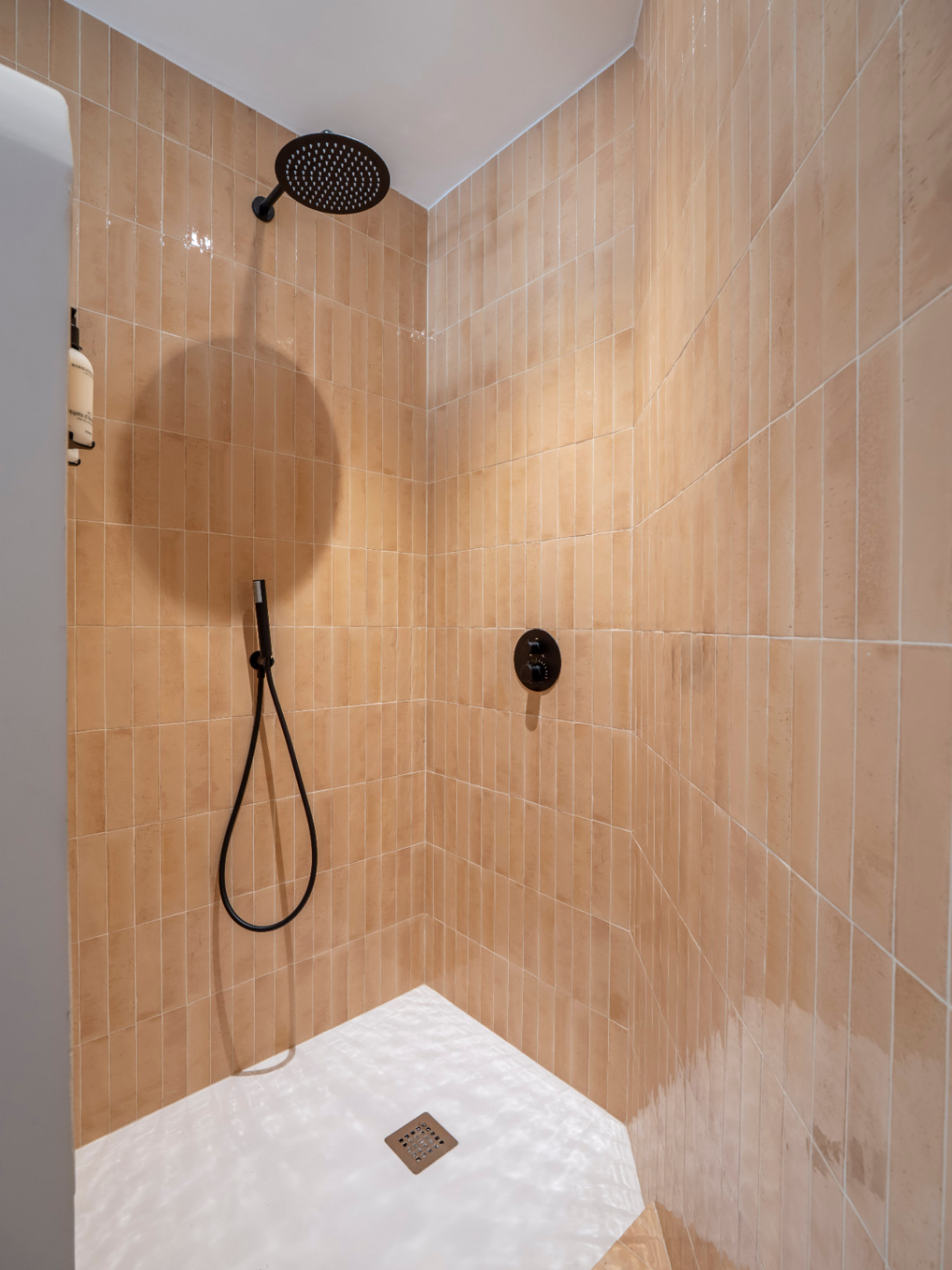 Detalle de ducha con azulejos verticales color terracota y grifería negra mate.