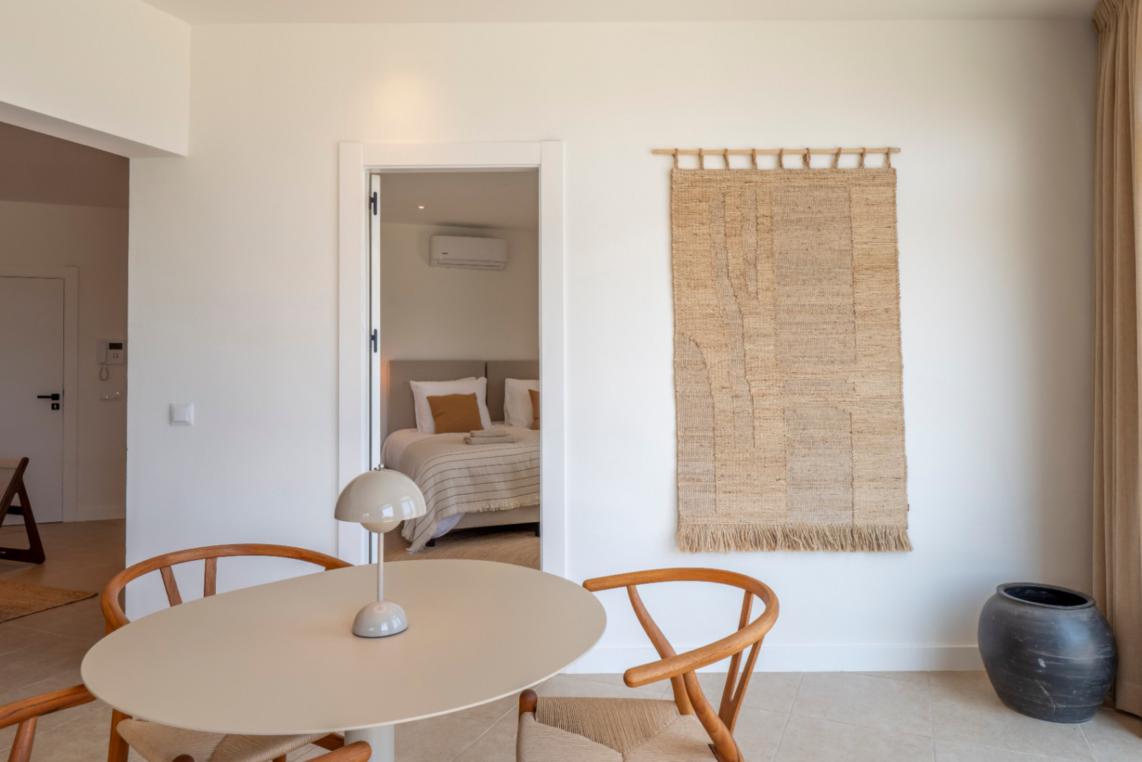 Detalle de interior con mesa redonda, sillas de madera y vista al dormitorio.