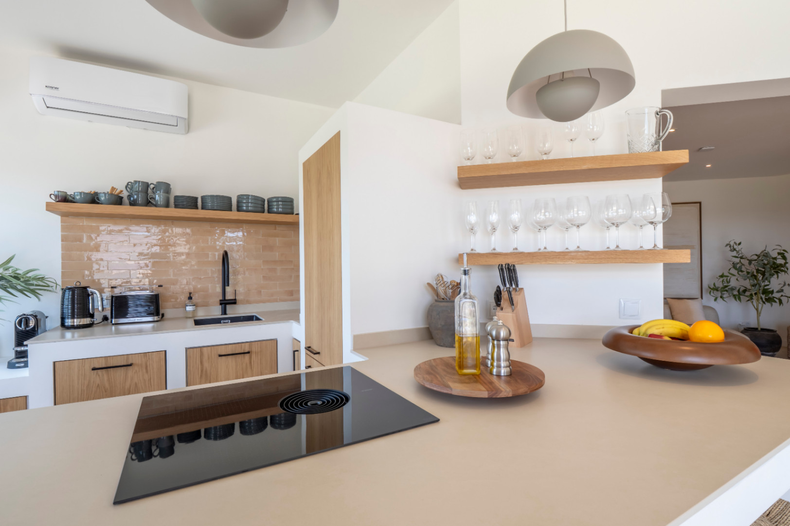 Detalle de la cocina con encimera beige, vitrocerámica negra y estantes de madera clara con cristalería.