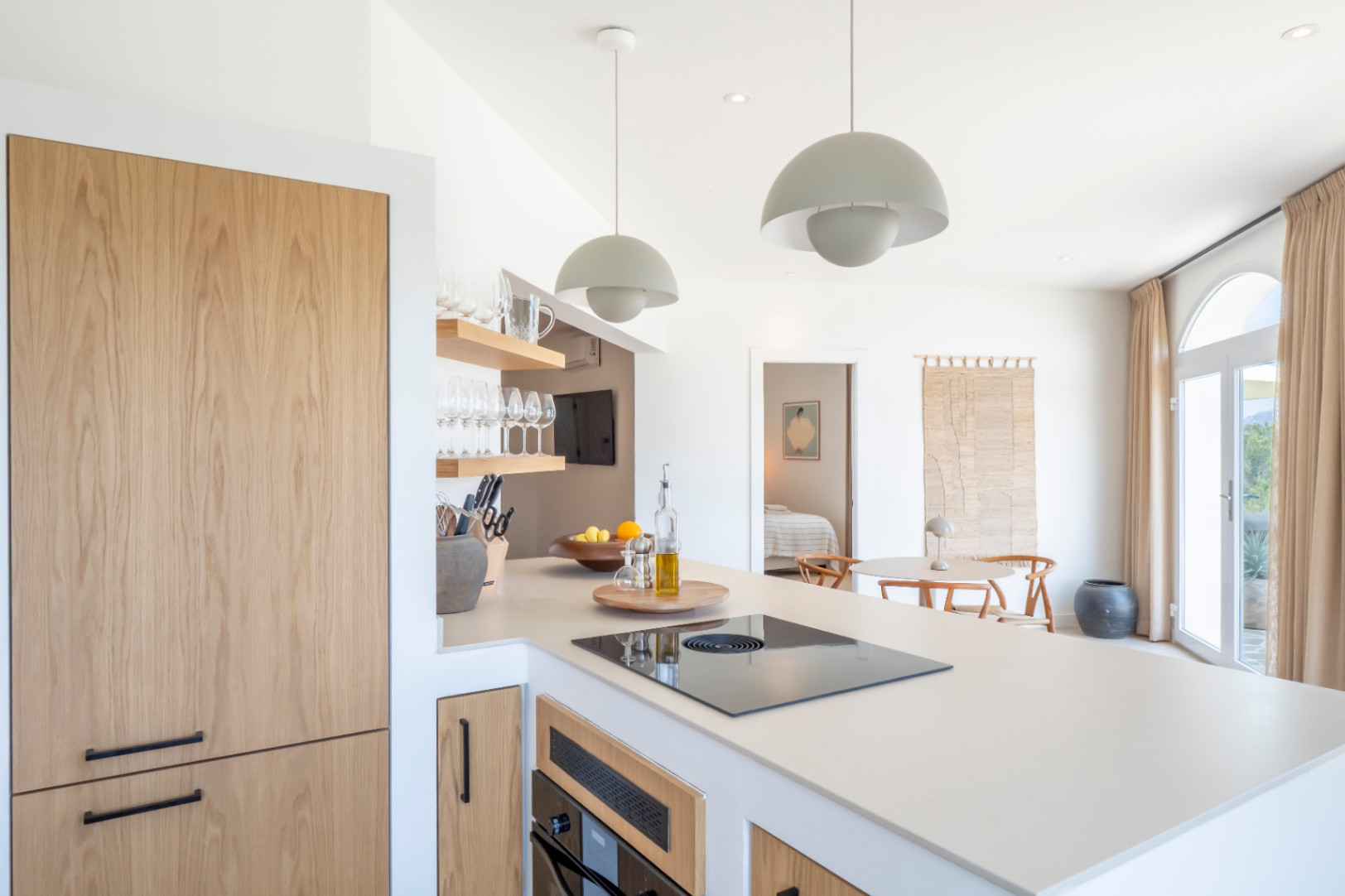 Detalle de la cocina con isla, electrodomésticos panelados en madera clara y estantes a la vista con cristalería.