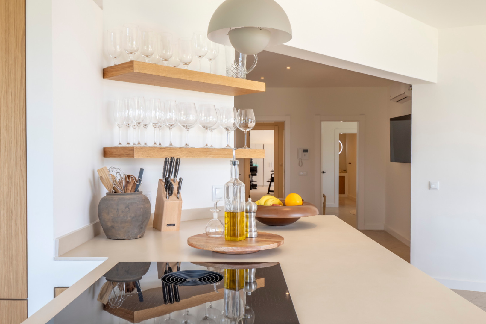 Detalle de la cocina: estantes de madera clara con copas, encimera beige con placa de inducción y decoración minimalista.