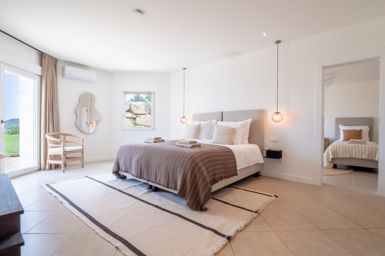 Dormitorio luminoso con cama doble, alfombra de rayas y vistas al jardín.