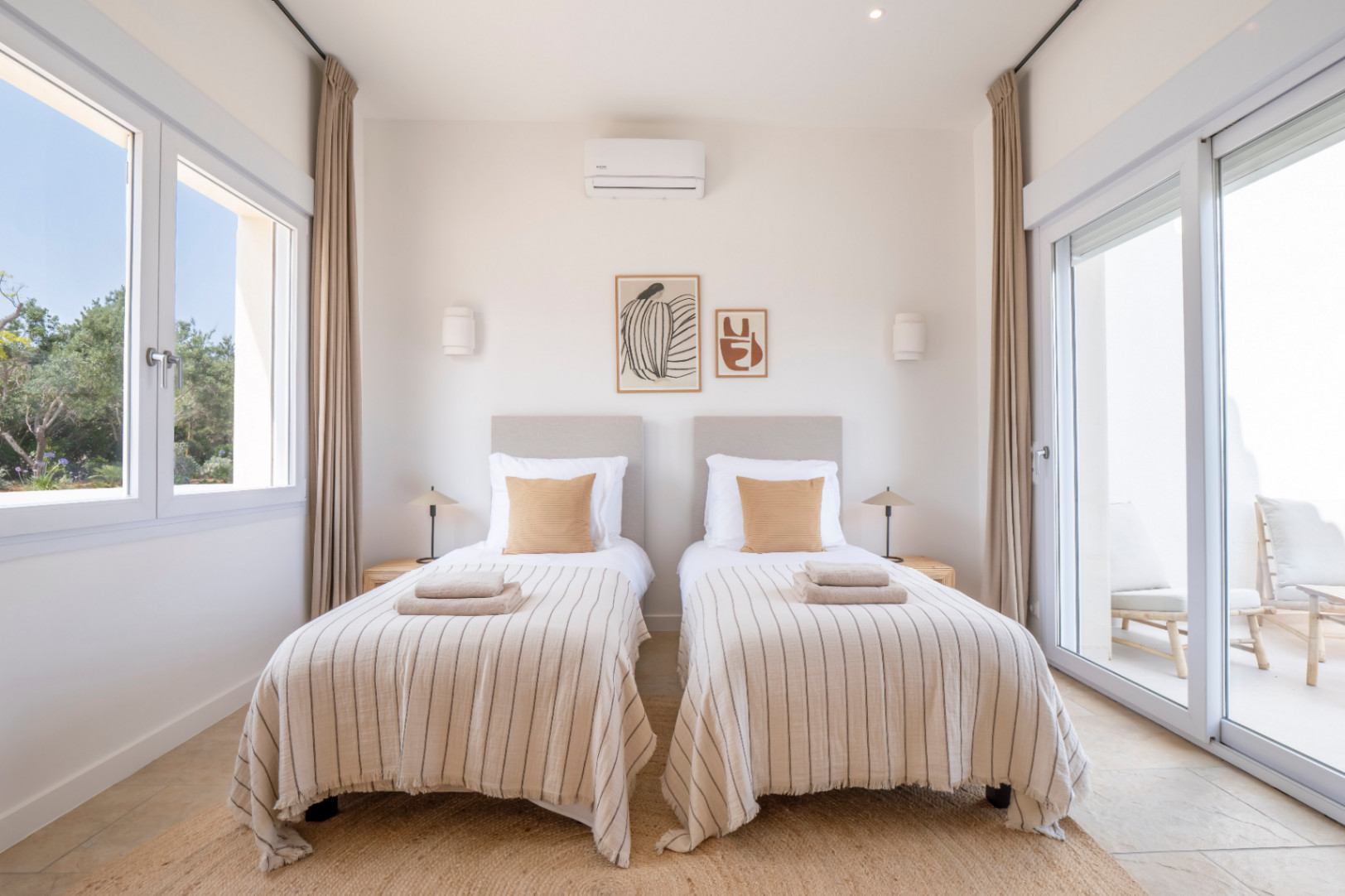 Dormitorio luminoso con dos camas individuales, ropa de cama a rayas y decoración minimalista. Acceso a terraza exterior.