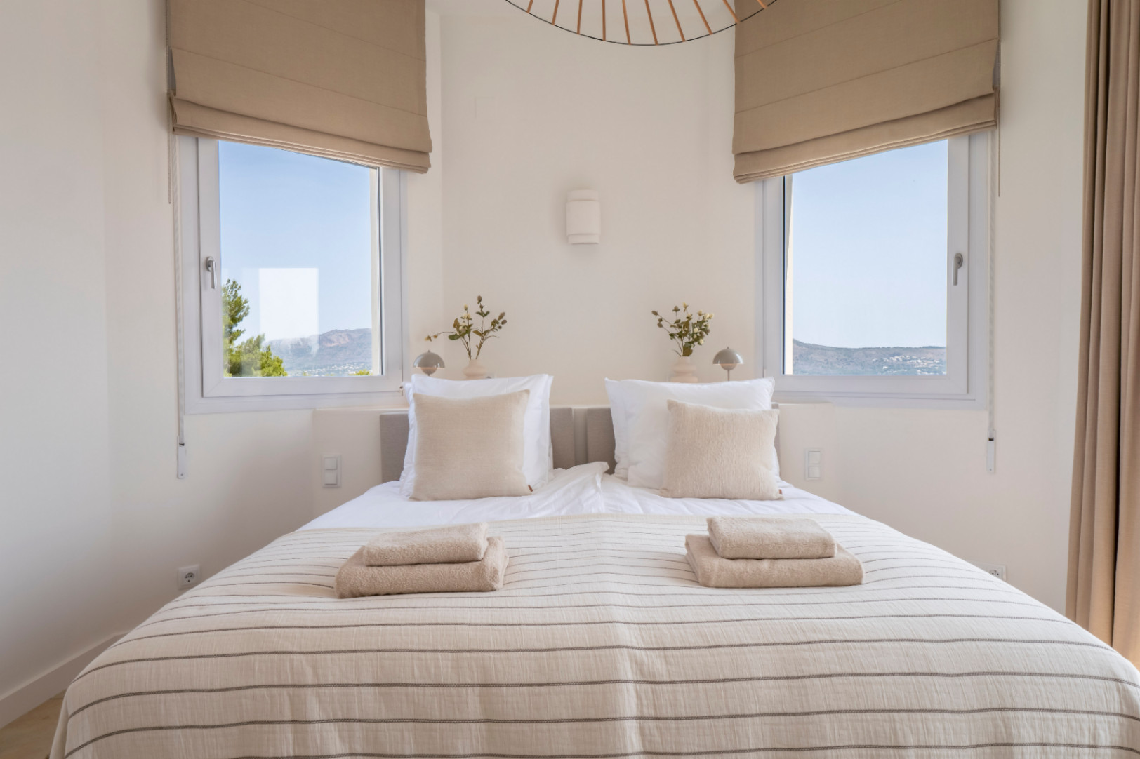 Dormitorio luminoso con dos ventanas que ofrecen vistas al exterior. Cama doble con ropa de cama a rayas y toallas.