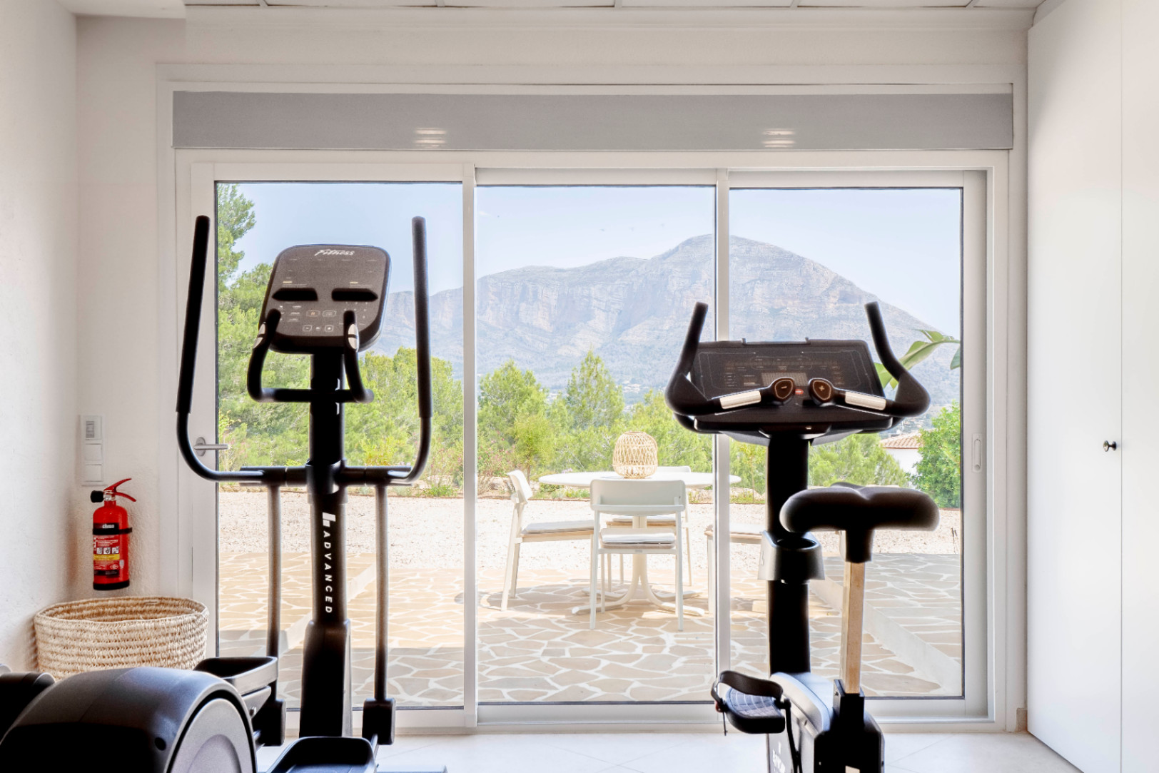Gimnasio luminoso con vistas a la montaña, equipado con bicicleta estática y elíptica.