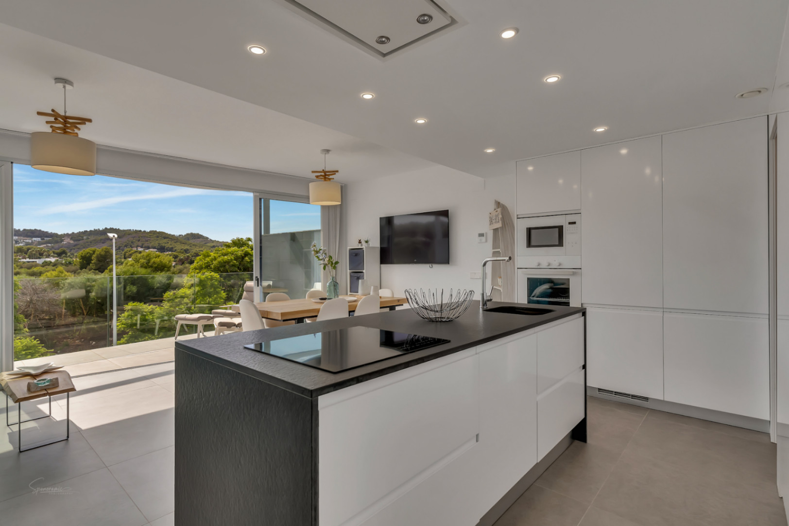 Cocina moderna de concepto abierto con isla central negra, electrodomésticos integrados y acceso directo a la terraza con vistas despejadas al entorno natural.