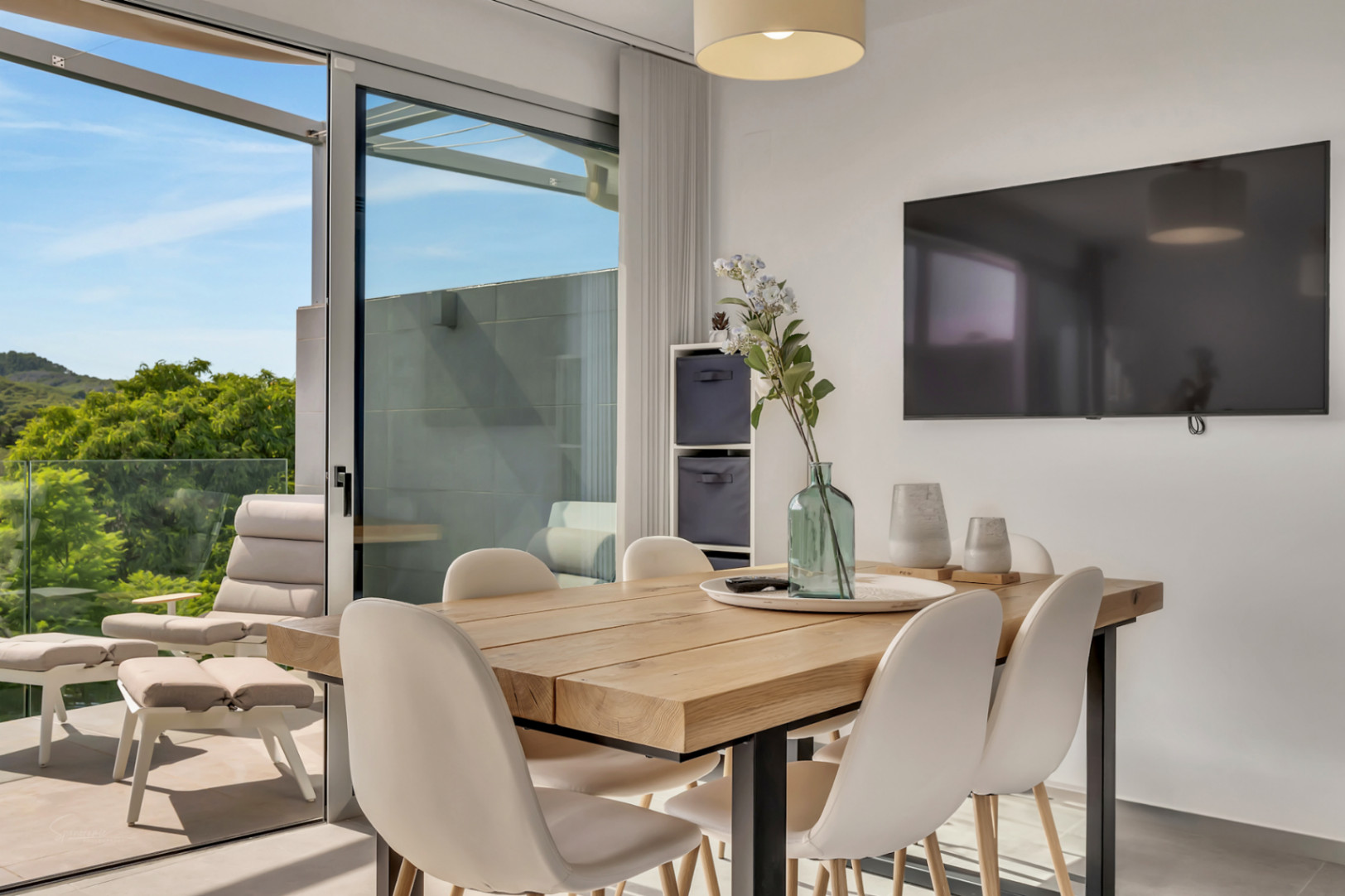 Comedor luminoso con mesa de madera maciza y acceso directo a un balcón con vistas despejadas a la vegetación y mobiliario de exterior.