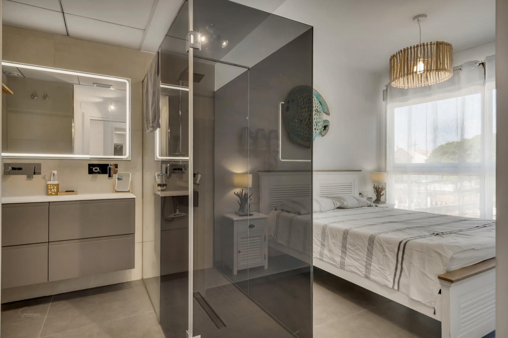 Dormitorio principal con baño integrado, destacando una ducha de obra con mampara de cristal ahumado y un lavabo suspendido con espejo retroiluminado.