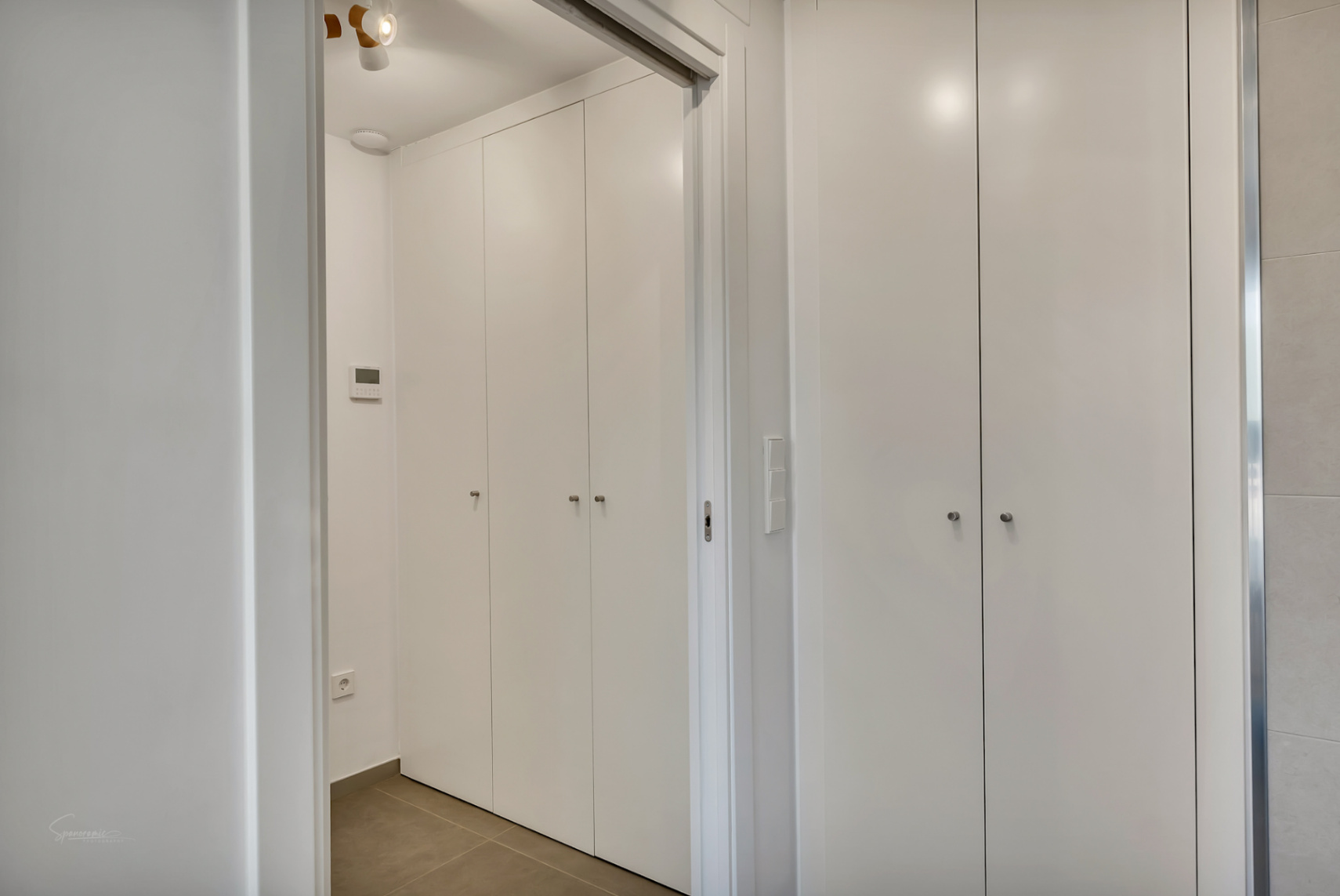 Pasillo moderno con armarios empotrados de suelo a techo en color blanco, tiradores minimalistas y suelos de gres porcelánico.