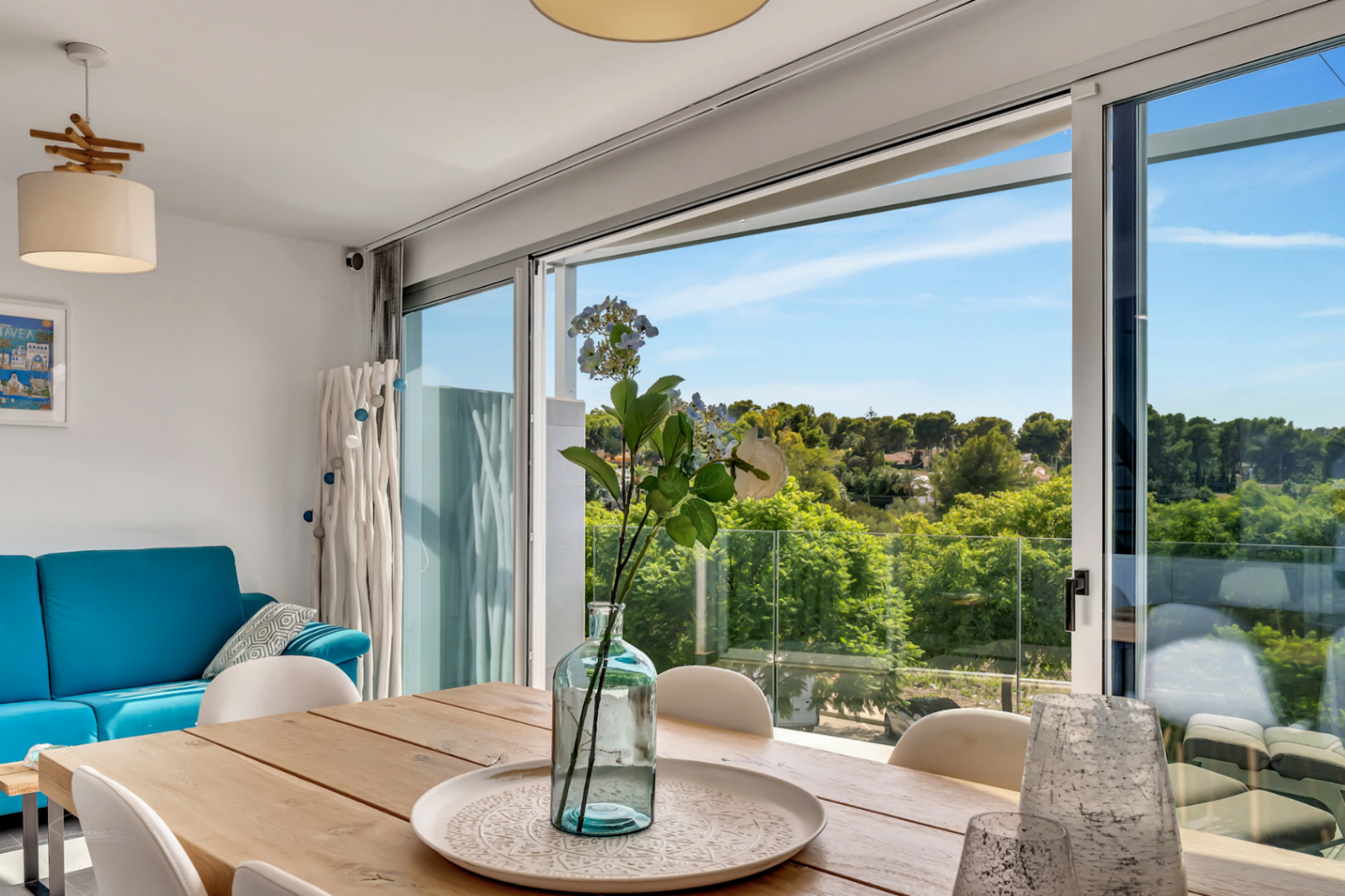 Salón-comedor luminoso con mesa de madera y amplios ventanales que ofrecen vistas despejadas a zonas verdes y acceso directo al balcón con barandilla de cristal.