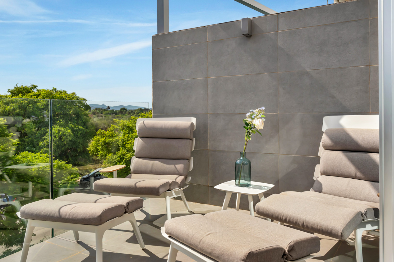 Terraza privada con mobiliario de diseño, barandilla de cristal y vistas despejadas a campos naturales y montañas.