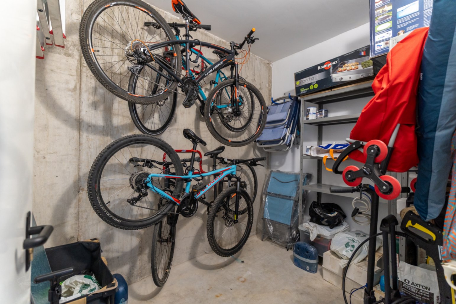 Trastero privado con paredes de hormigón visto, equipado con soportes de pared para bicicletas y estanterías metálicas para un almacenamiento organizado.