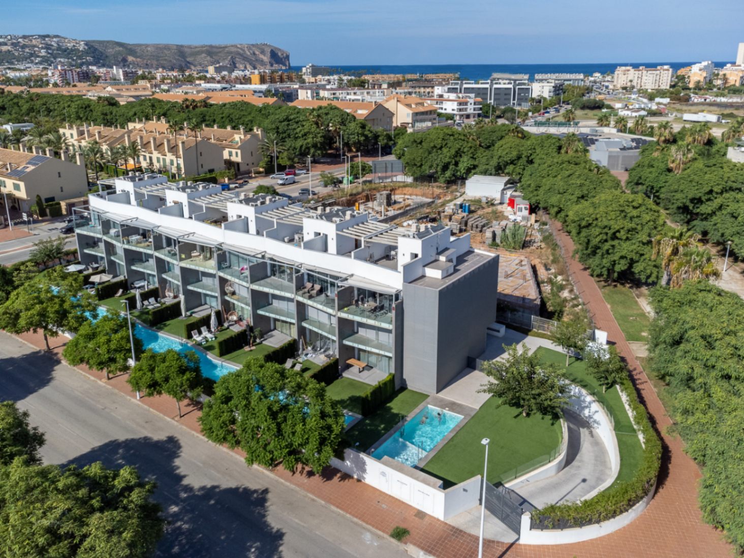 Vista aérea del complejo residencial moderno con arquitectura contemporánea, piscinas comunitarias, zonas verdes y vistas panorámicas hacia la costa y la montaña.