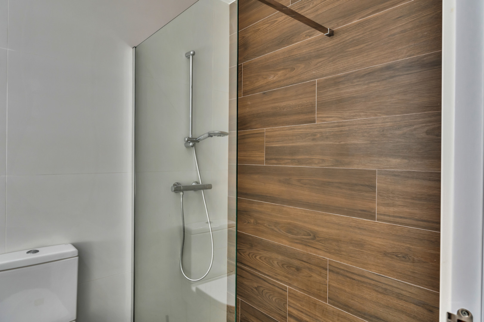 Baño moderno con ducha italiana, mampara de cristal fija y pared revestida en gres cerámico con efecto madera natural.