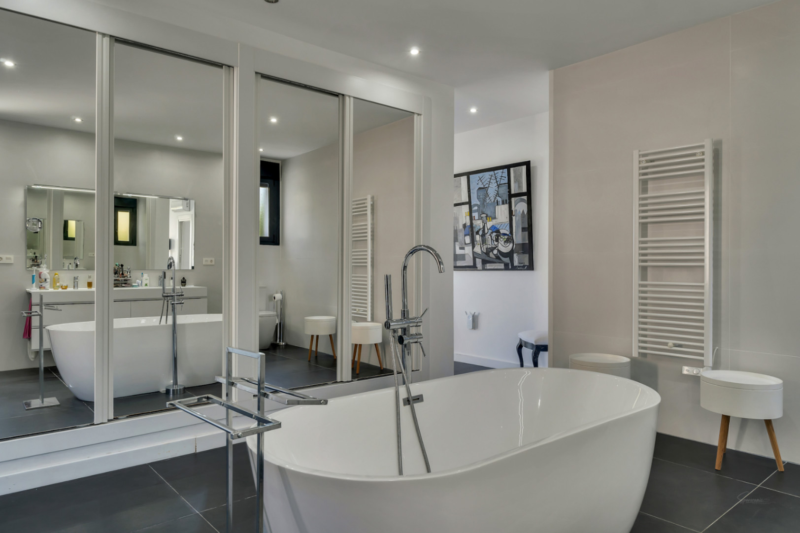 Baño principal con bañera exenta, grifería de pie cromada y amplios armarios con puertas de espejo que multiplican la luminosidad y el espacio.