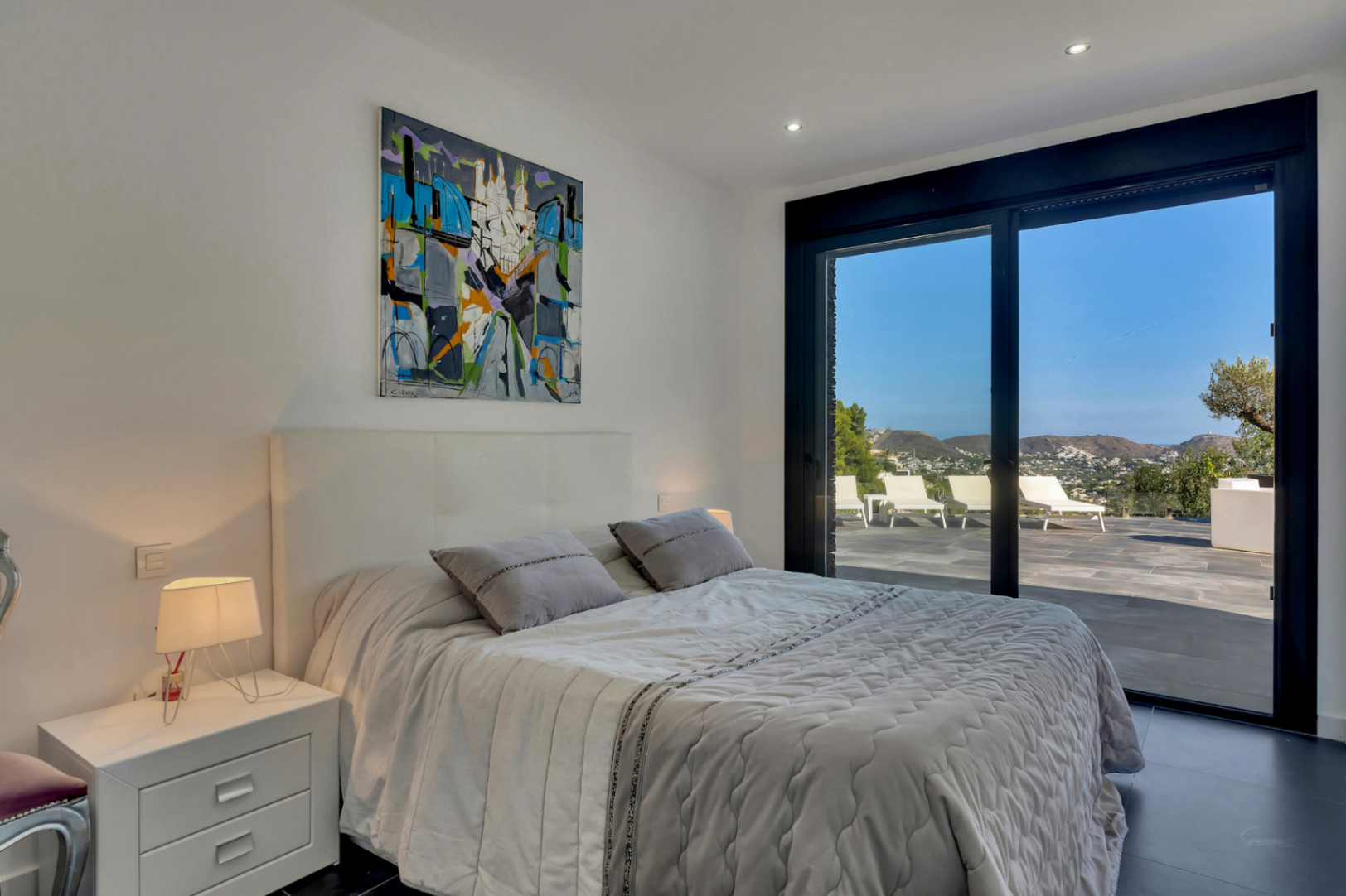 Dormitorio moderno con acceso directo a la terraza privada. Destacan los ventanales de suelo a techo con vistas despejadas a la montaña y el mar, integrando el exterior.