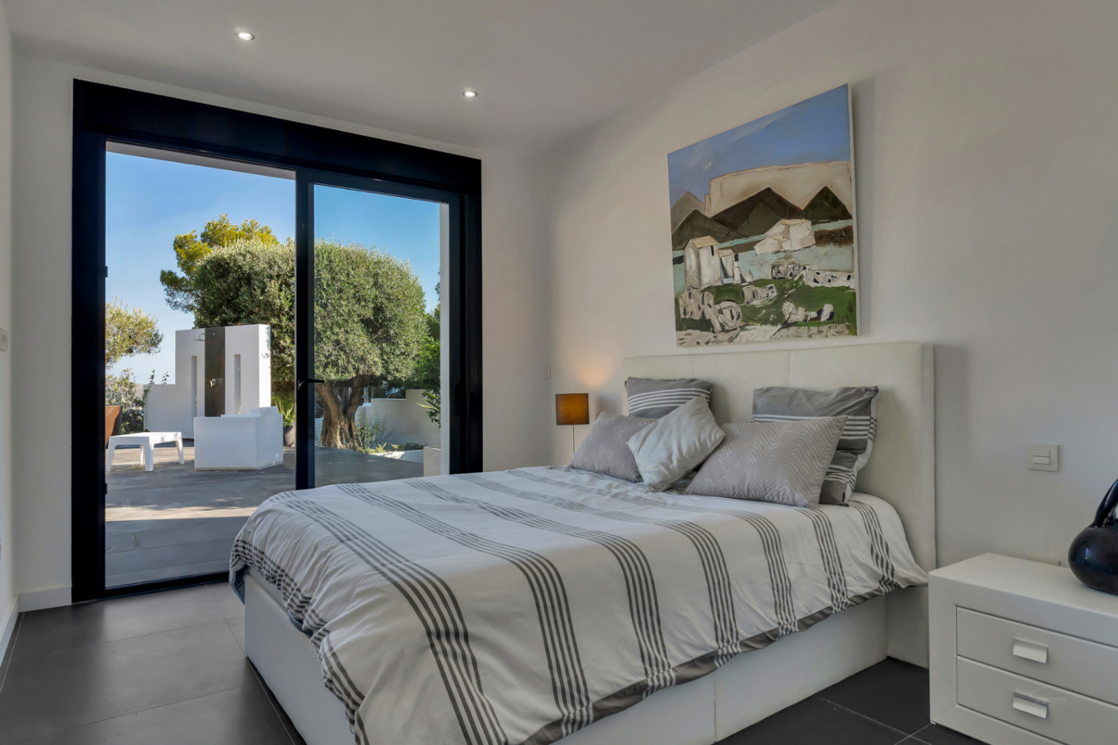 Dormitorio moderno con acceso directo a la terraza, ventanales de carpintería negra, suelos cerámicos oscuros e iluminación empotrada en el techo.