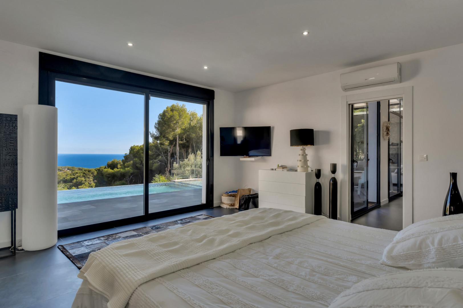 Dormitorio principal con ventanales de suelo a techo que ofrecen vistas directas al mar y la piscina. Incluye suelos oscuros, aire acondicionado y acceso directo a la terraza.