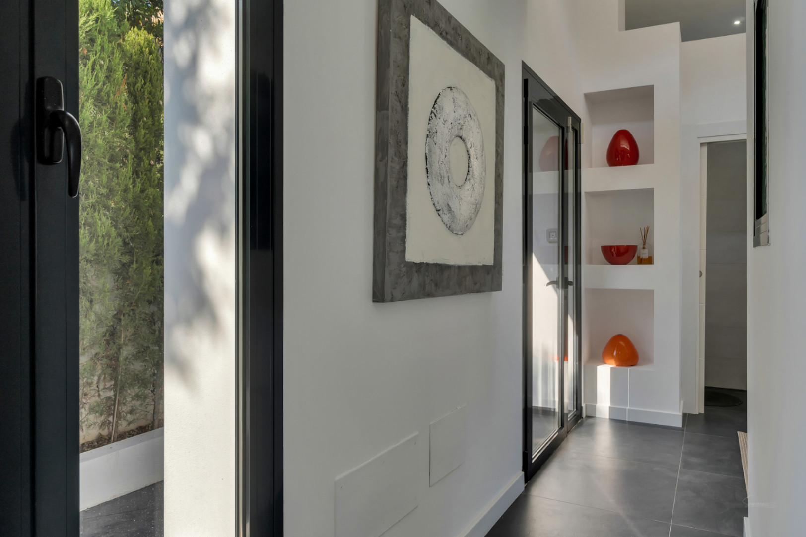 Pasillo de diseño moderno con suelos de gres oscuro, hornacinas decorativas integradas y carpintería negra que permite la entrada de luz natural.