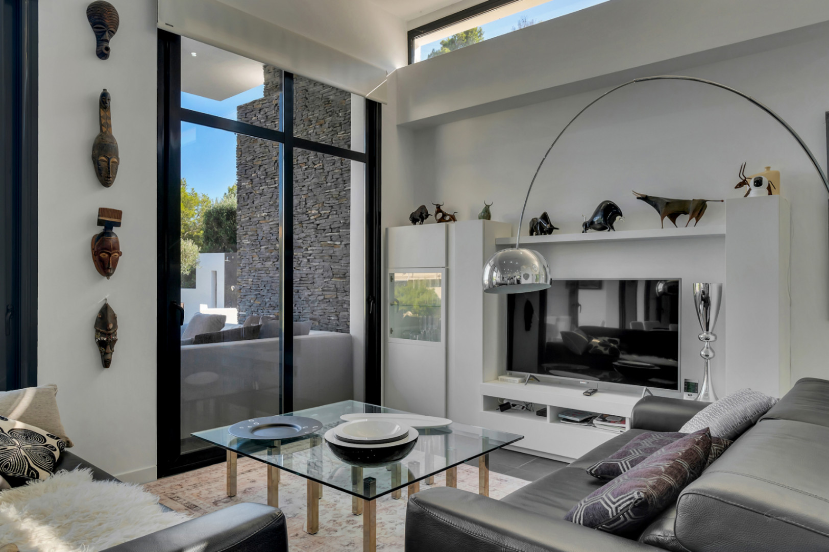 Salón de diseño con techos de gran altura, ventanales de suelo a techo y zona de estar equipada con sofás de cuero y una icónica lámpara de arco.