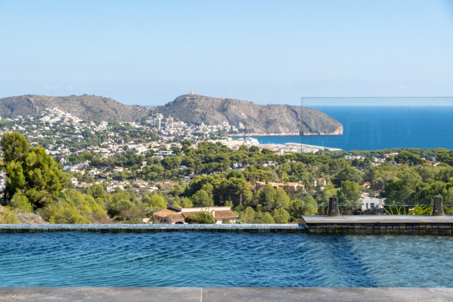 Vistas panorámicas desde la piscina infinita hacia el mar Mediterráneo y el Cap d'Or, con barandilla de cristal que maximiza la visibilidad del entorno costero.