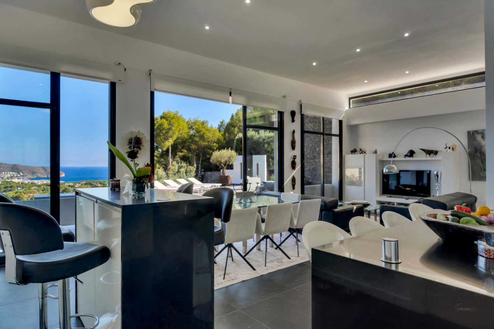 Zona de día diáfana con techos altos, cocina con isla y barra, comedor y salón integrados con vistas panorámicas al mar y acceso directo a la terraza.