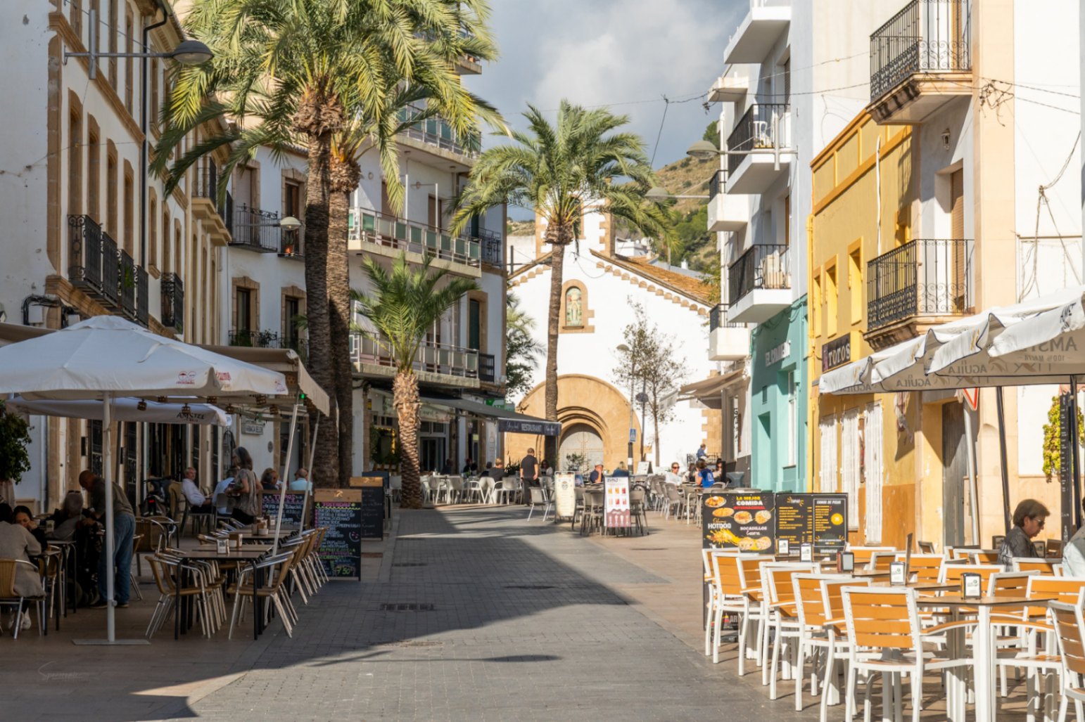 Calle peatonal en el casco antiguo de Jávea con terrazas, palmeras y arquitectura tradicional, reflejando el entorno inmediato de la vivienda.
