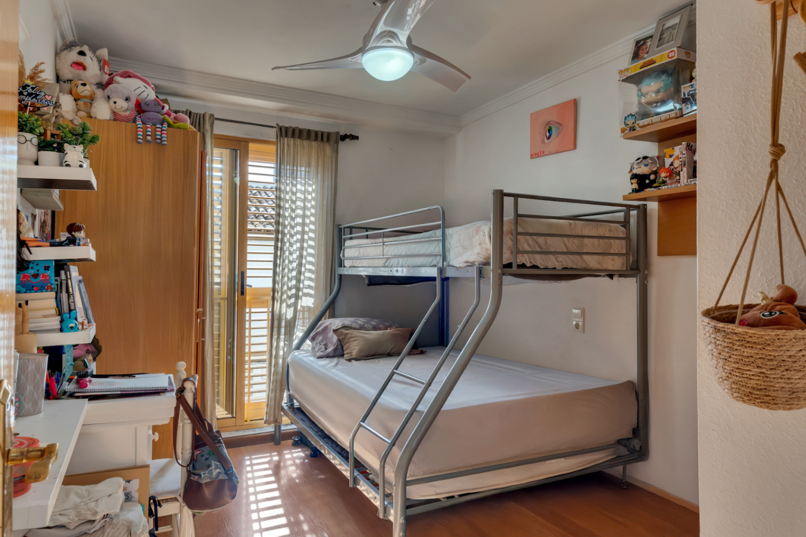 Dormitorio secundario con litera metálica, suelos de madera y ventilador de techo. Dispone de acceso directo al exterior mediante puertas correderas con contraventanas de madera.